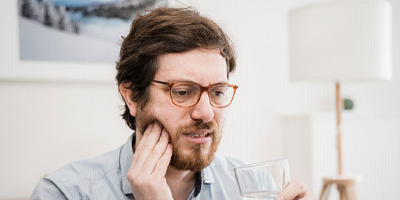 Bearded man with glasses drinking water and rubbing toothache