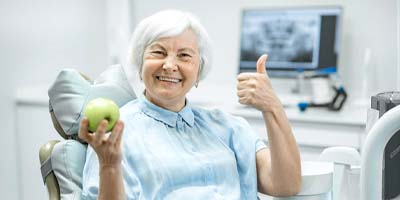 Woman with dental implants in Carmichael, CA giving thumbs up and holding apple