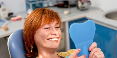 Woman holding mirror, admiring her new implant dentures