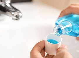 Pair of hands pouring blue mouthwash over sink