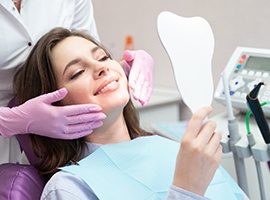 Happy patient using mirror to admire her new dental implant restorations