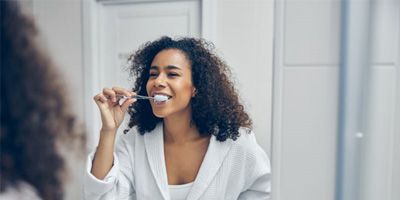 Woman brushing her teeth in front of bathroom mirror