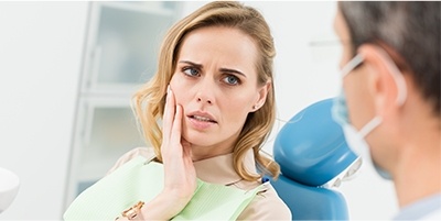 Woman in dental chair holding jaw