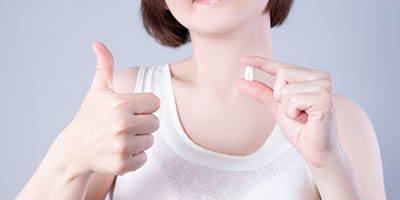 Woman holding tooth, giving thumbs up for surgical tooth extractions in Carmichael