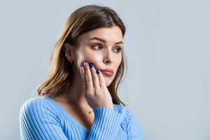 Woman in blue sweater rubbing her jaw